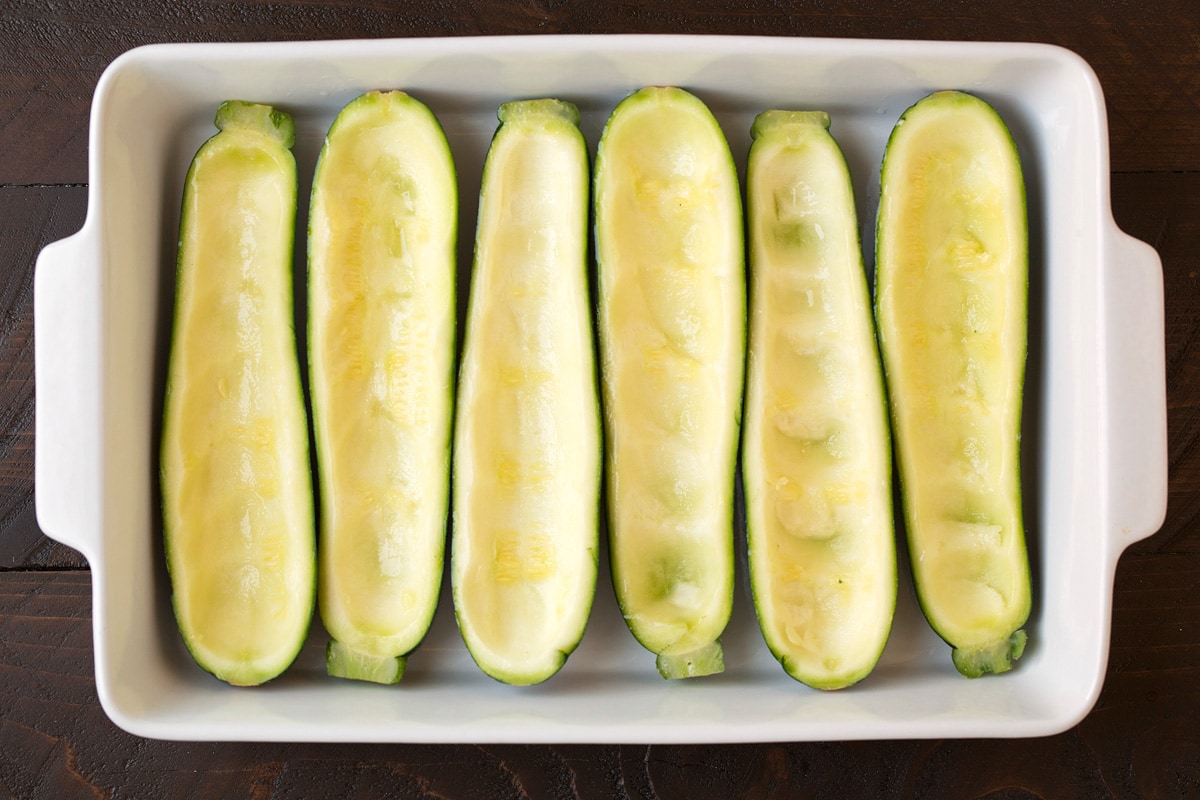 Hollowed out zucchini made into boats in a baking dish before adding filling.