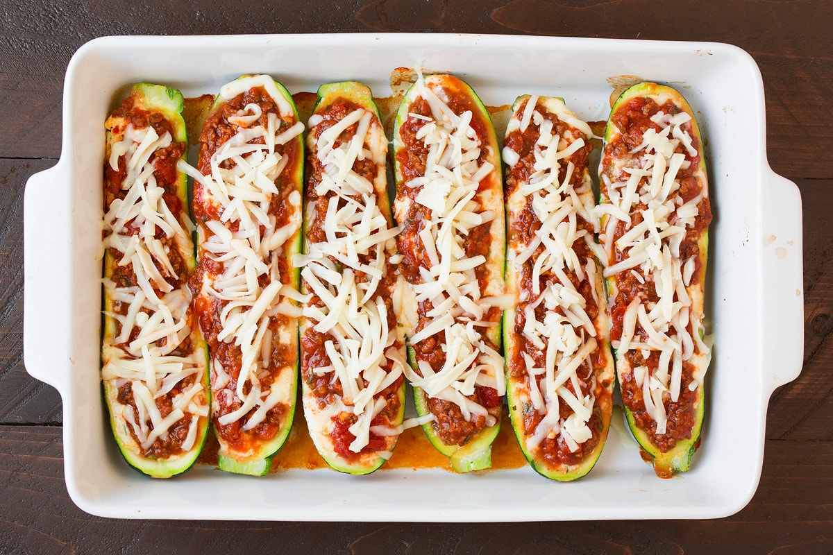 Adding shredded cheese over sauce layer in zucchini boats.