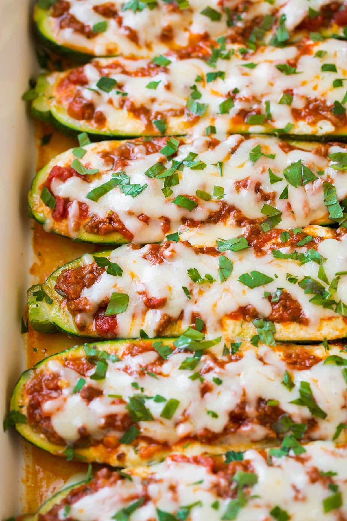 Close up image of Lasagna Zucchini Boats in a row in baking dish.