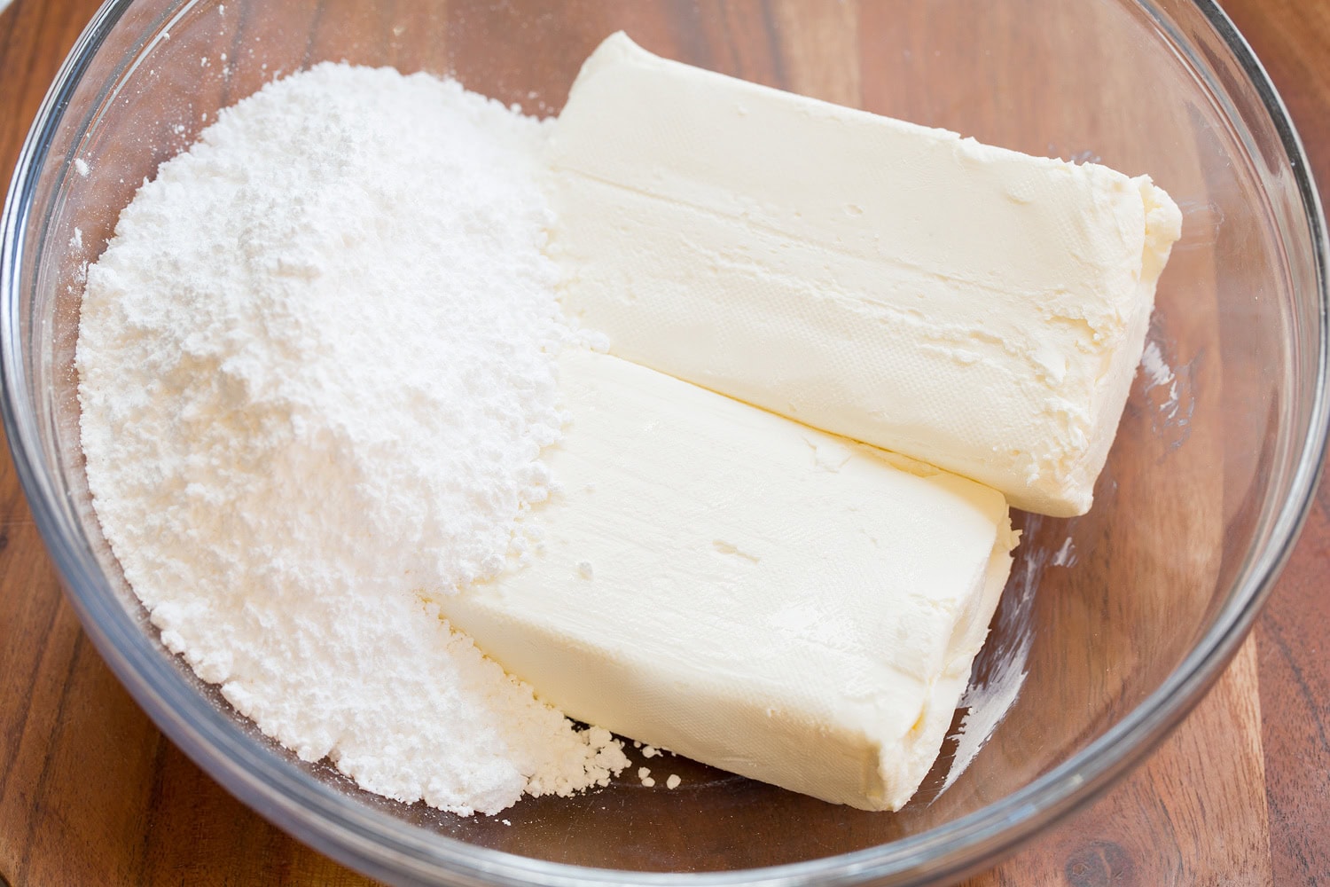 Cream cheese and powdered sugar in glass mixing bowl.