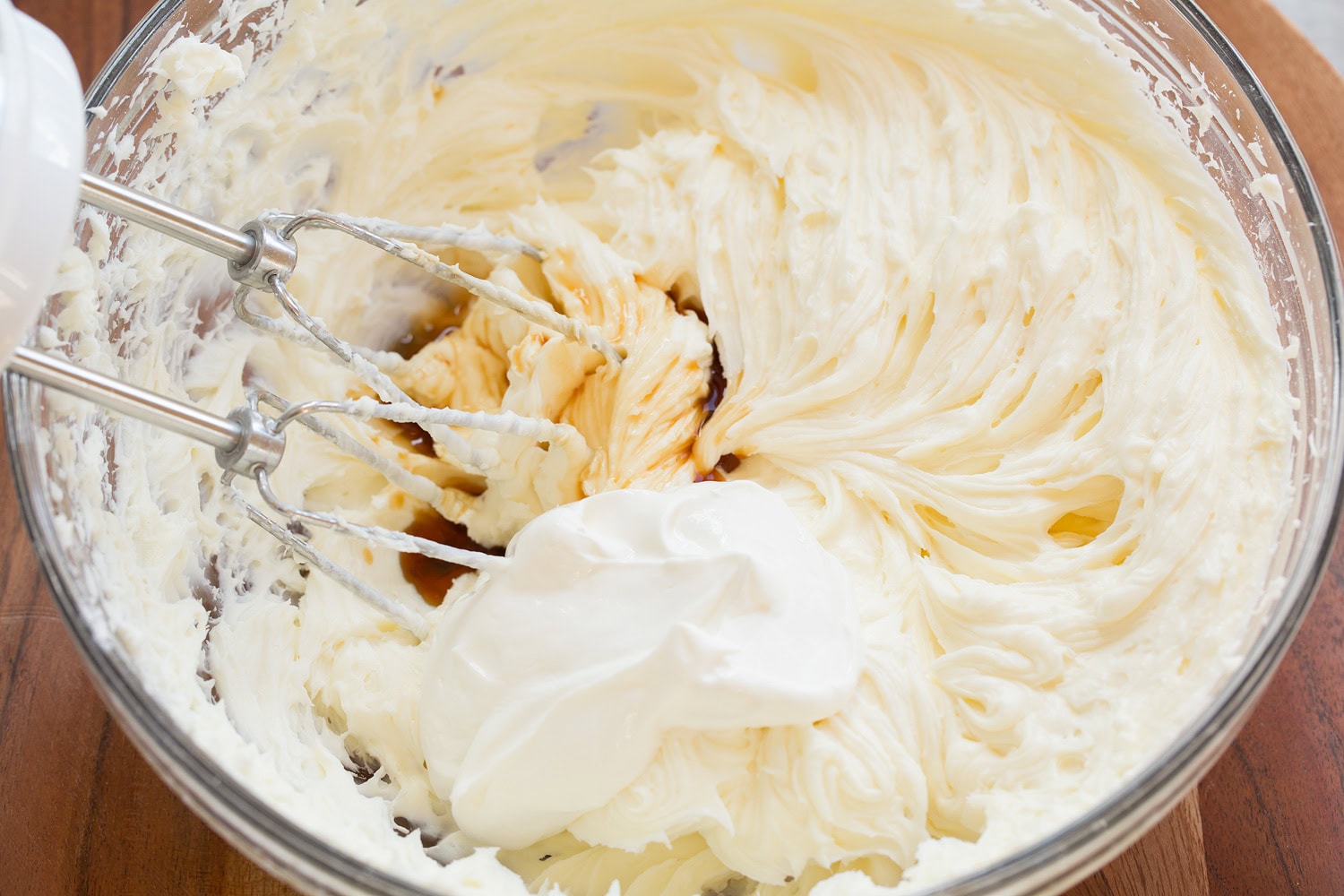 Sour cream and vanilla added to cream cheese mixture in glass bowl.