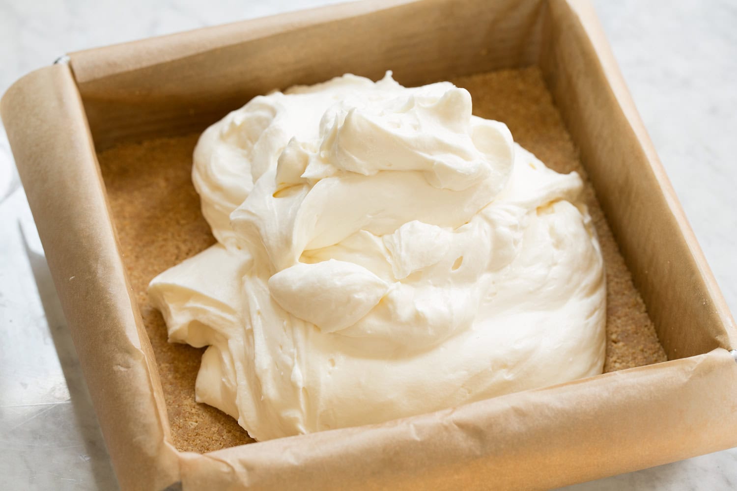 No bake cheese cake topping over graham cracker crust in pan before spreading.