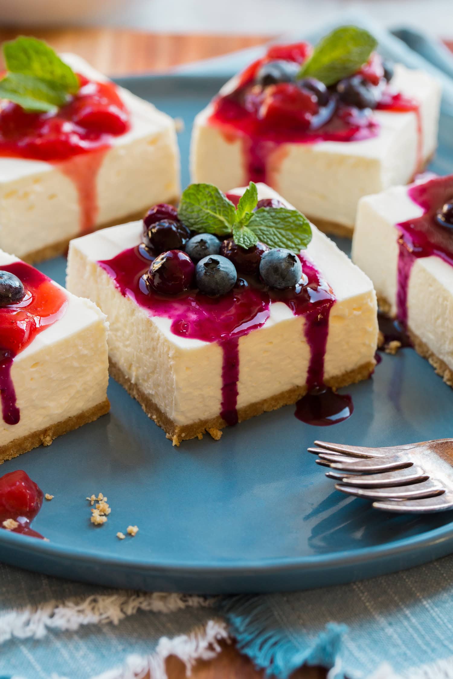 No Bake Cheesecake bars shown with strawberry sauce and blueberry sauce, plus mint.