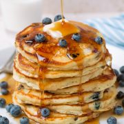 Pouring syrup over stack of homemade blueberry pancakes