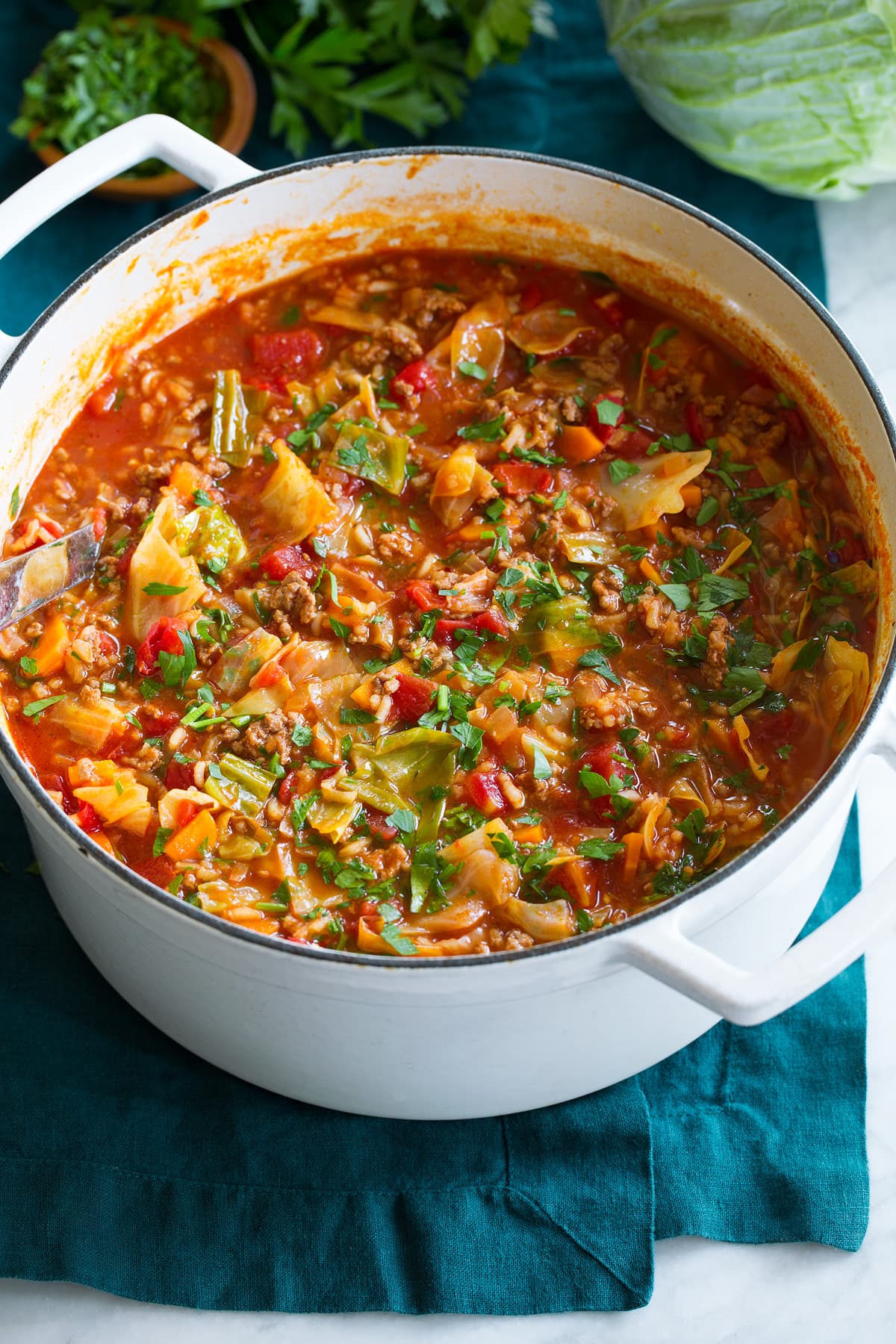 Cabbage Roll Soup shown in a large white pot on a blue cloth.