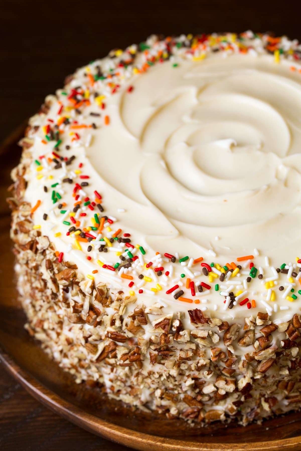 A whole round spice cake without any slices cut. It's covered with a cream cheese frosting, chopped pecans around the edges and fall sprinkles around the top.