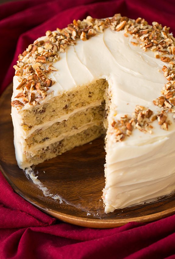 Butter Pecan Cake on a wooden platter. A large slice is removed from cake to show interior. 