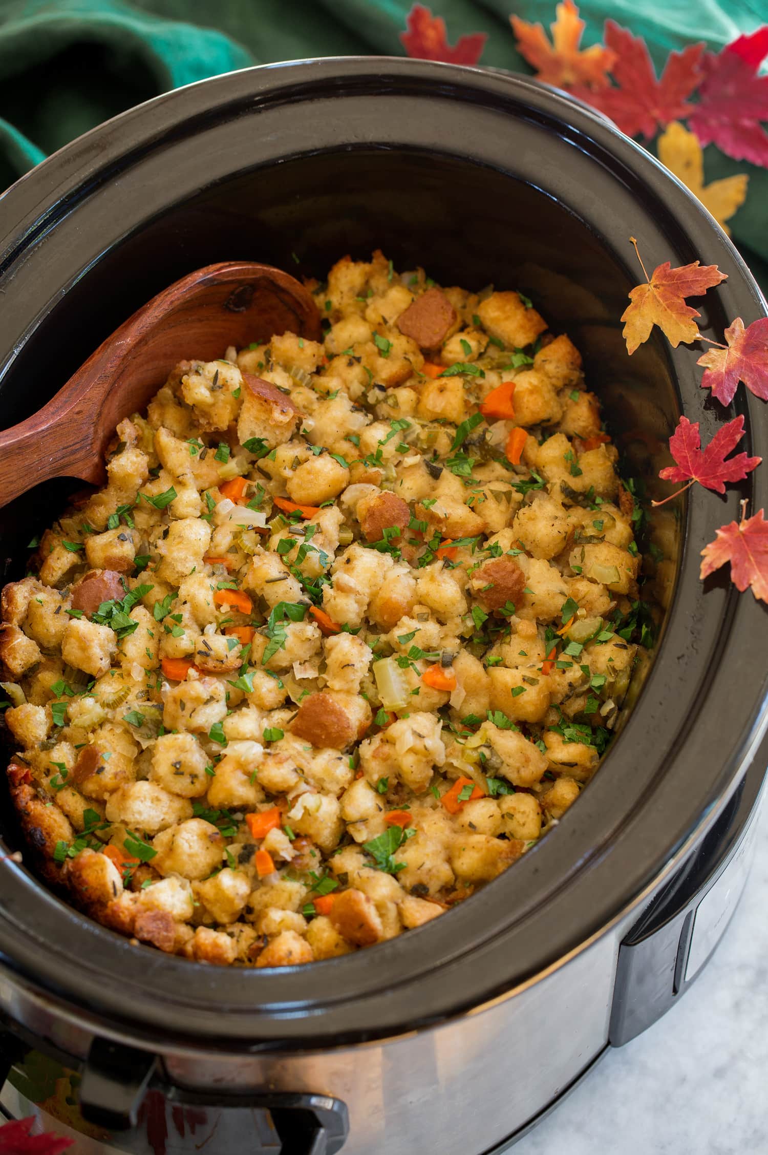 Stuffing in a crockpot with decorative fall leaves and a green cloth to the side.