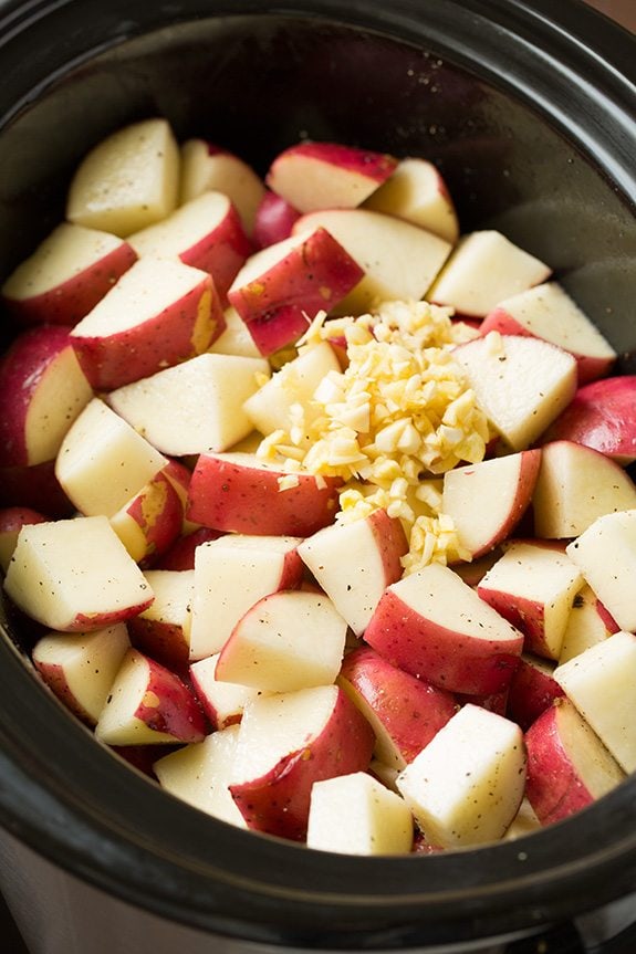 Showing how to make mashed potatoes in a slow cooker. Diced potatoes and garlic are being added.