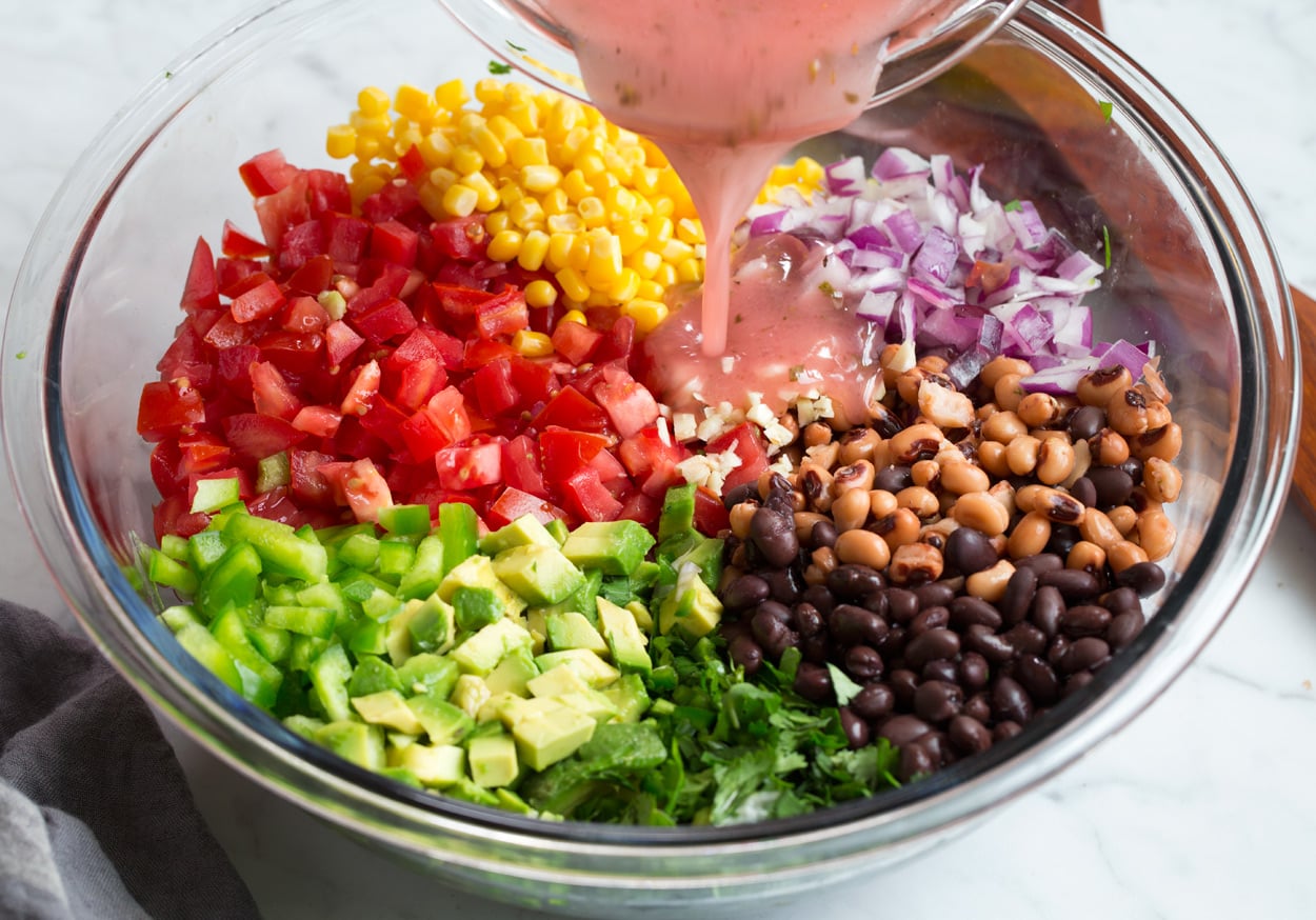 Cowboy Caviar adding dressing to veggies and beans in mixing bowl