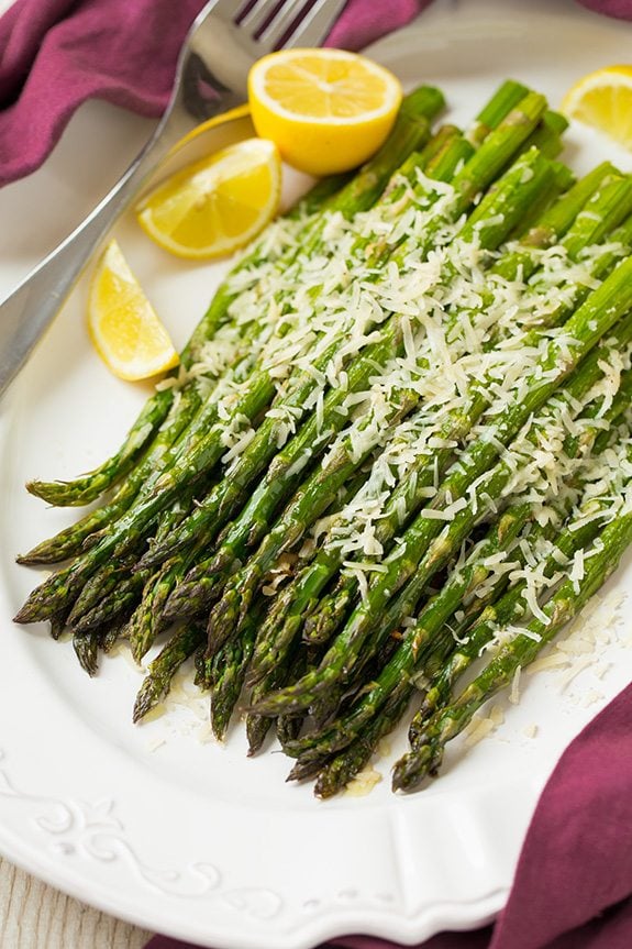 Roasted Parmesan Asparagus  on a white platter with lemon wedges