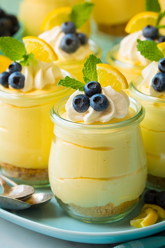 Soft, light and delicious this lemon mousse is the ultimate spring summer dessert. Made with a graham cracker base and a smooth, silky and luscious whipped cheesecake topping it's pretty hard to resist! #cookingclassy #lemon #cheesecake #mousse Lemon mousse in a glass topped with whipped cream, blueberries and lemon