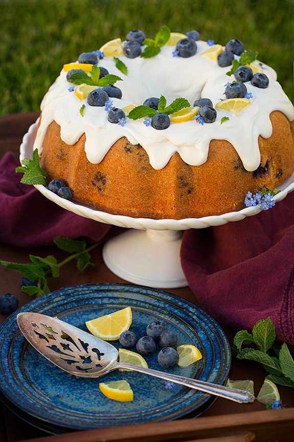 Lemon Blueberry Bundt Cake on cake stand behind blue plate