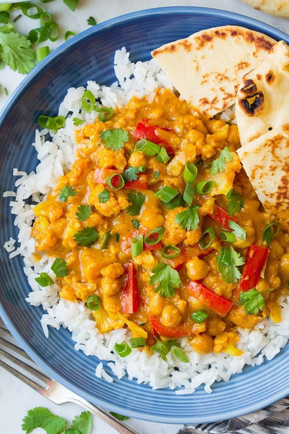 Vegetable curry over rice in a blue bowl. Ingredients include cauliflower, red bell pepper, onion, cilantro and a curry sauce.