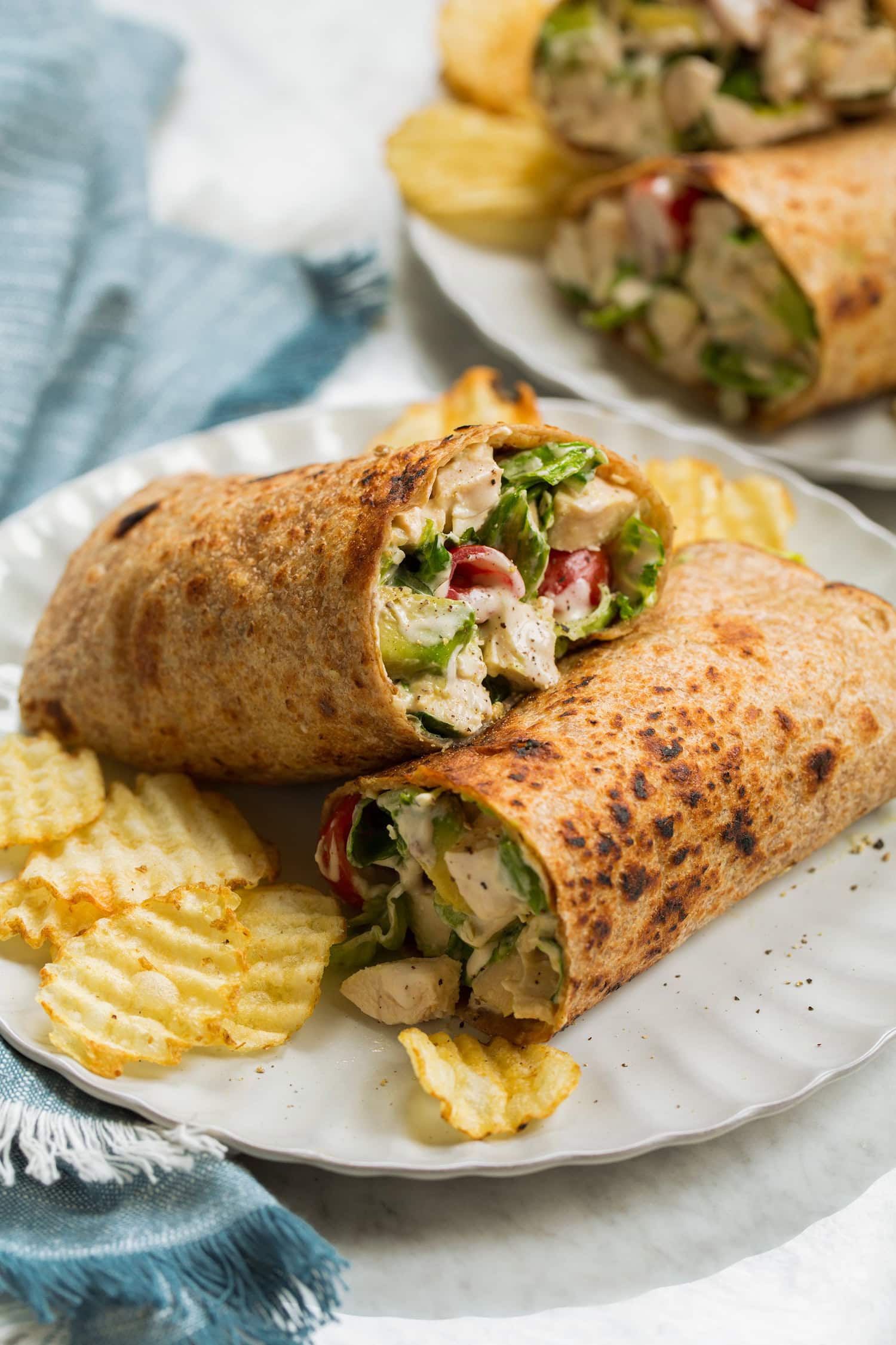 Chicken Caesar Wrap Chicken caesar wrap with avocado and tomato shown served with potato chips.