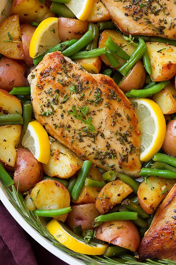 Garlic and herb seasoned chicken breasts in a skillet with green beans, potatoes and lemons.