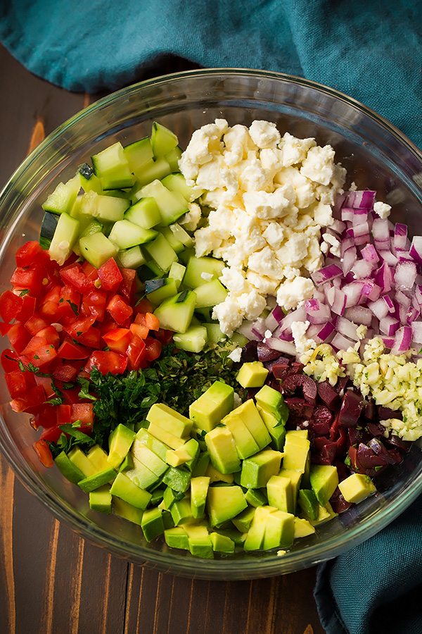 Grilled Salmon with Avocado Greek Salsa and Orzo Greek salsa ingredients in a glass mixing bowl. Includes tomatoes, cucumbers, avocado, feta, red onion, garlic, olive and herbs.