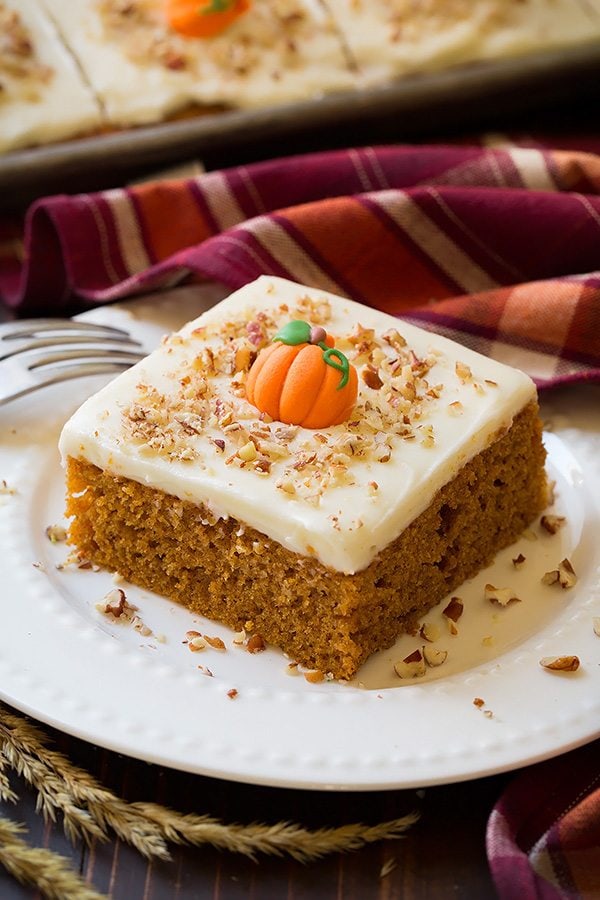 Slice of Pumpkin Sheet Cake with Cream Cheese Frosting served on a white plate. Decorated on top with pecans and candy pumpkin in the center.