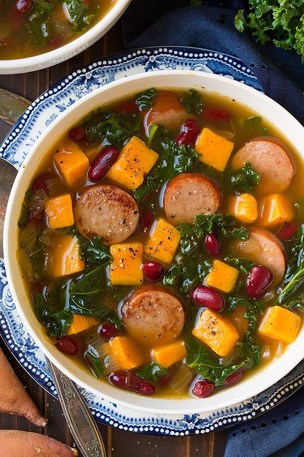 Turkey Sausage, Kale and Sweet Potato Soup in a white serving bowl set over a vintage blue plate.