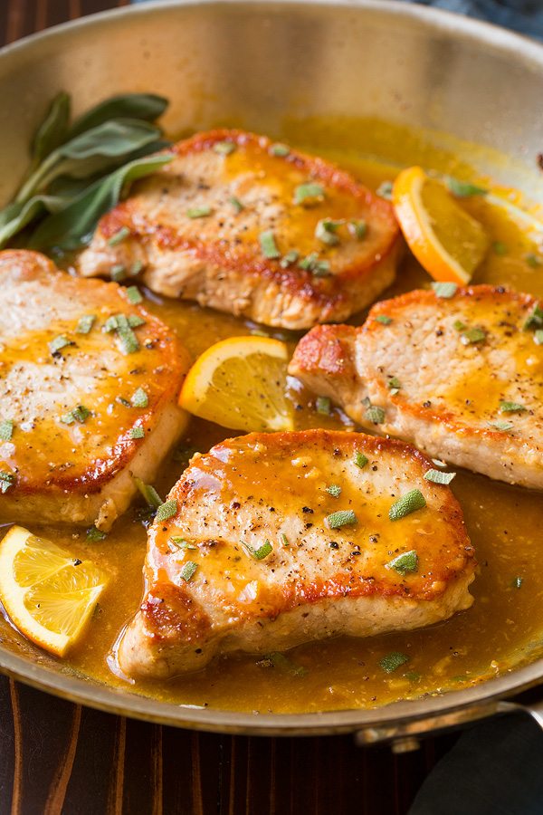 Boneless pork chops in skillet with orange and herb sauce.