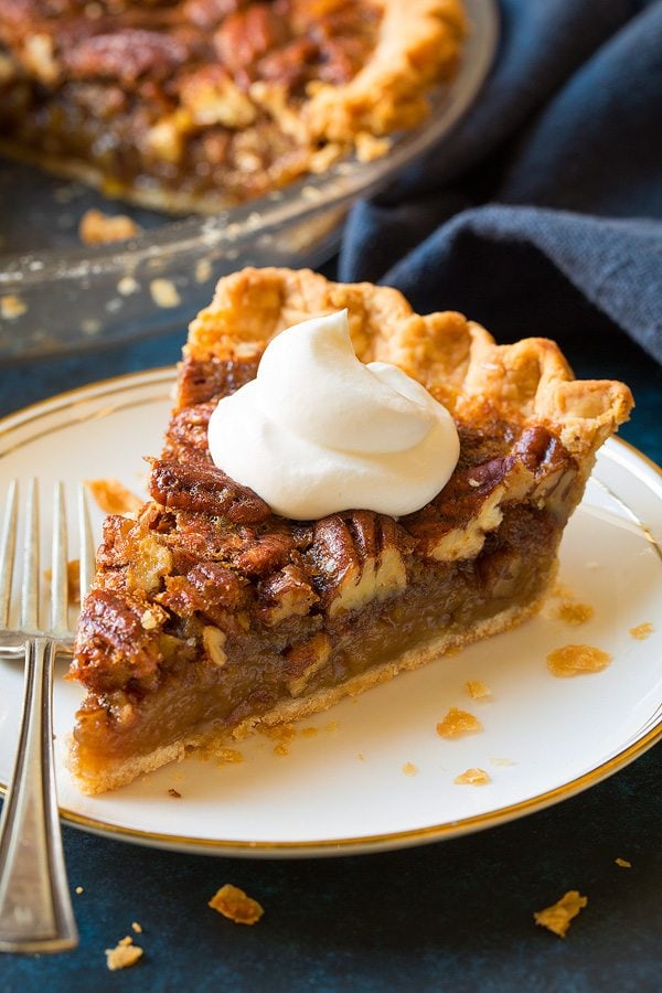 Slice of pecan pie on a white dessert plate. Pie is topped with whipped cream.