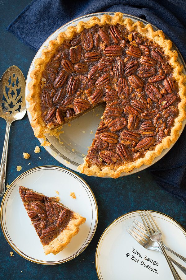 Overhead image of whole pecan pie in pie dish and a slice to one side. Pie is resting on a blue surface.