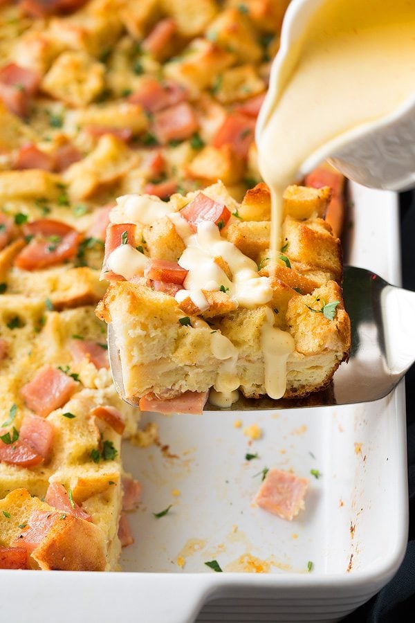 Pouring hollandaise sauce over eggs benedict casserole.