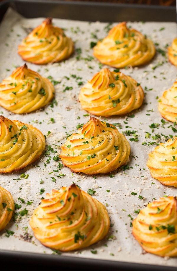 Duchess potatoes garnished with parsley and parmesan on a baking sheet.