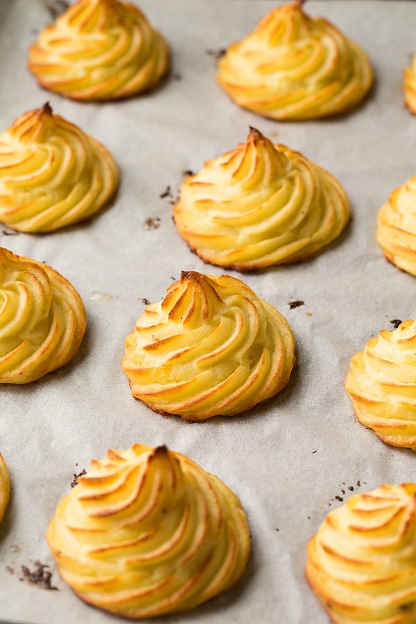 Duchess potatoes on a parchment paper lined baking sheet after baking.