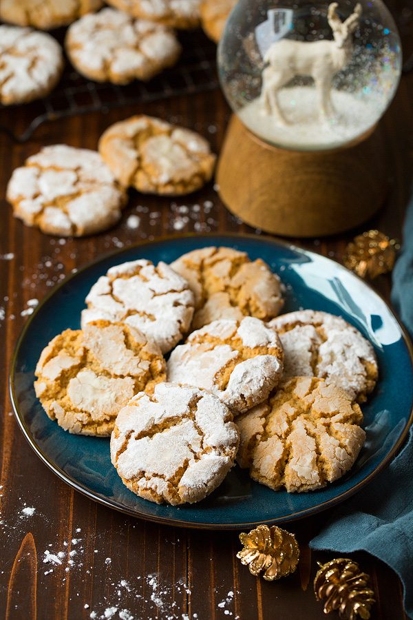 Seven Peanut Butter Crinkle Cookies on a blue plate set over a dark wooden surface. There is a snow globe in the background.