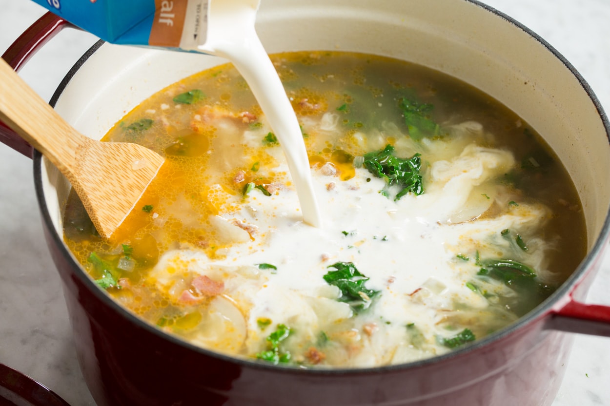 Pouring half and half into zuppa toscana soup in pot.