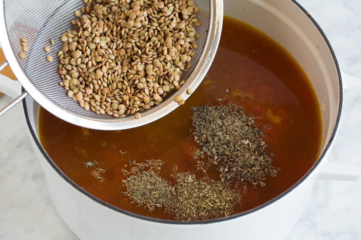 adding lentils and herbs into a pot of soup