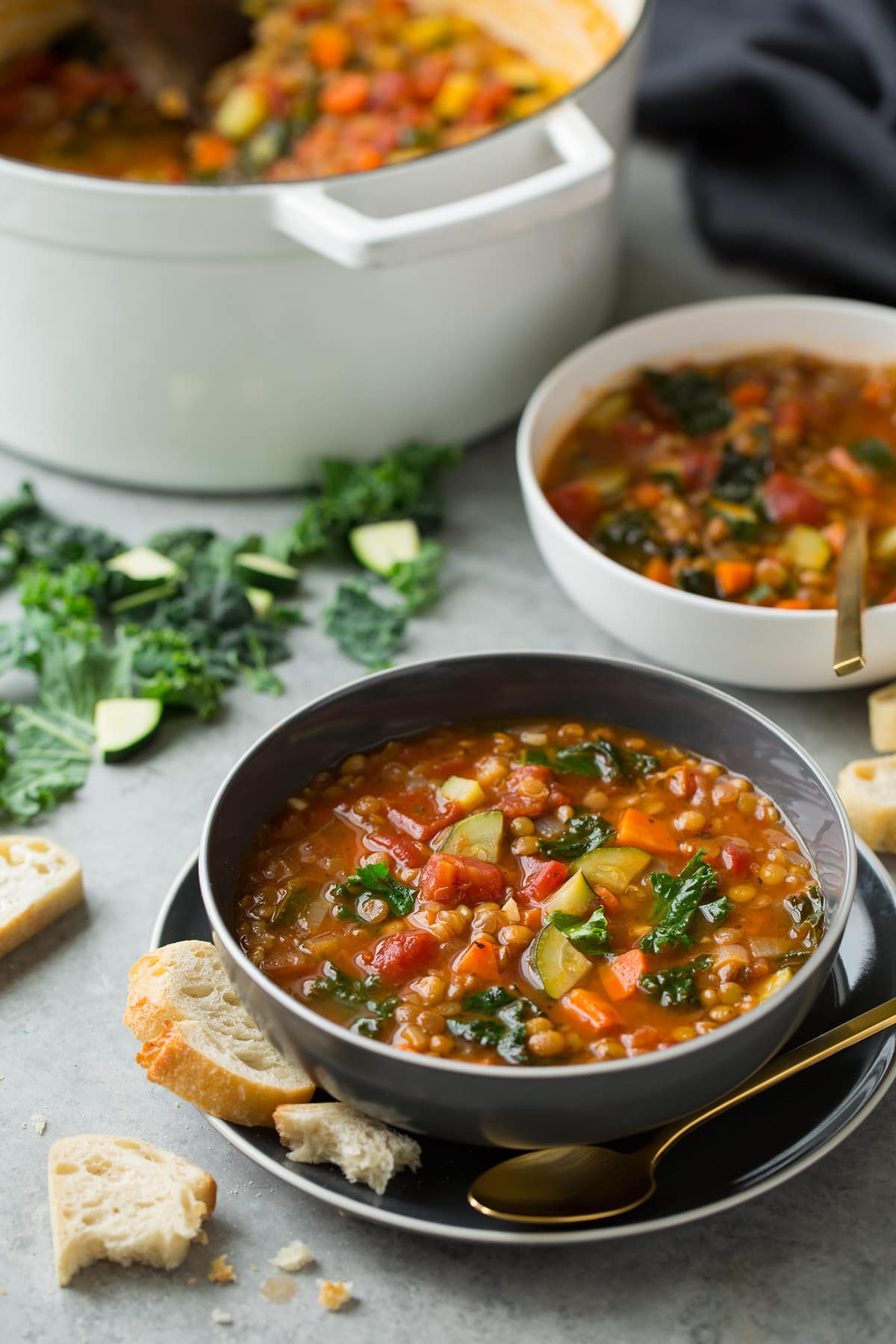 Lenti Soup shown here in an individual serving in a grey bowl set over a grey plate with a second serving in the background