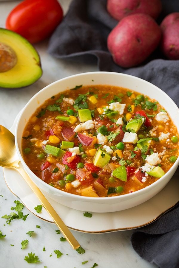 Quinoa and Vegetable Stew in a white bowl set over a gold rimmed white plate.