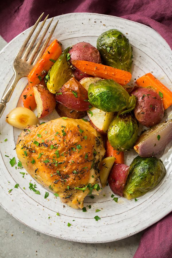 Roasted chicken thigh and roasted vegetables on a white serving plate.