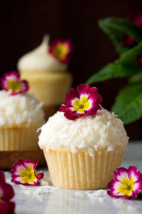 Coconut Cupcake with coconut buttercream frosting topped with shredded coconut and pink flower