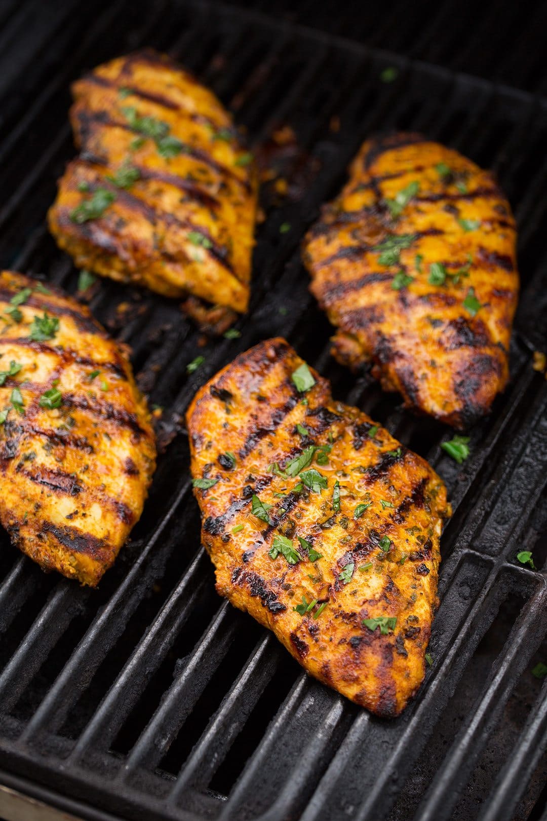 Four boneless skinless chicken breasts cooking on grill.