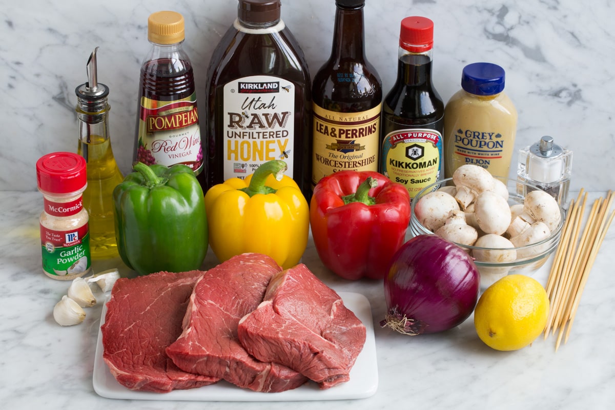 Ingredients needed to make steak kebabs shown here including steaks, bell peppers, red onion, garlic, lemon, dijon mustard, soy sauce, Worcestershire, honey, red wine vinegar, olive oil, garlic powder. 