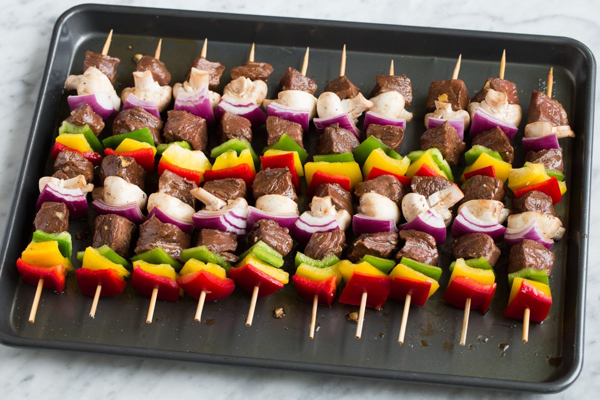Kebabs ingredients threaded onto skewers, shown before grilling aligned on a baking sheet.
