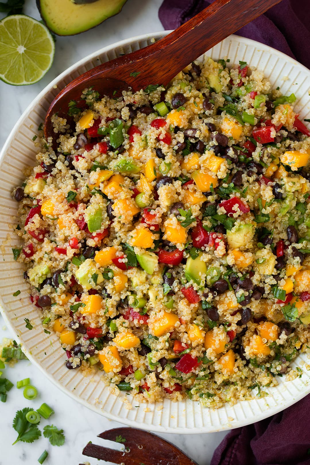 Quinoa Salad with Black Beans Mangoes and Avocados Overhead image of Quinoa Salad in a large white ceramic bowl, with wooden spoon for serving.