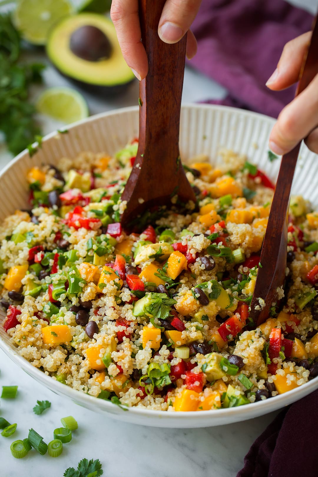 Quinoa Salad with Black Beans Mangoes and Avocados Tossing quinoa black bean salad in a large bowl with wooden spoons.