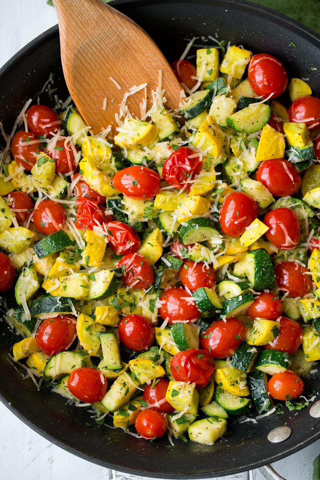 Overhead image of sauteed zucchini, squash and tomatoes in a large dark skillet.