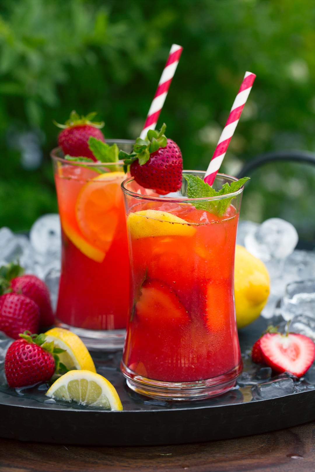 two glasses of Strawberry Lemonade on tray with lemon wedges and fresh strawberries 