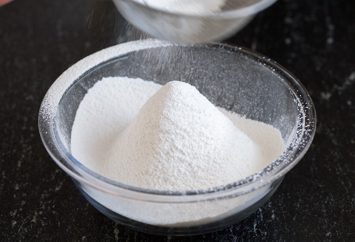 Sifting cake flour into a glass mixing bowl.