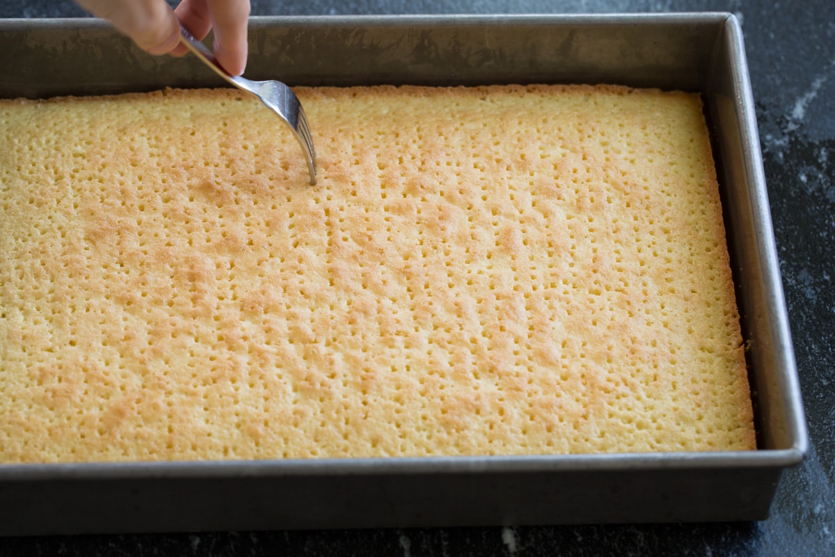 Poking baked tres leches cake with a fork all over.