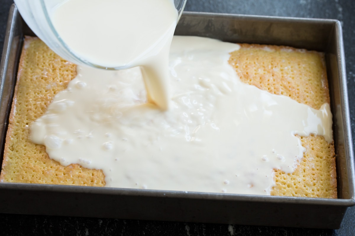 Pouring milk mixture over poked cake.