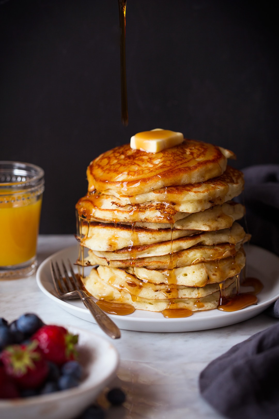 Stack of pancakes on a plate. Syrup is being poured over the top.