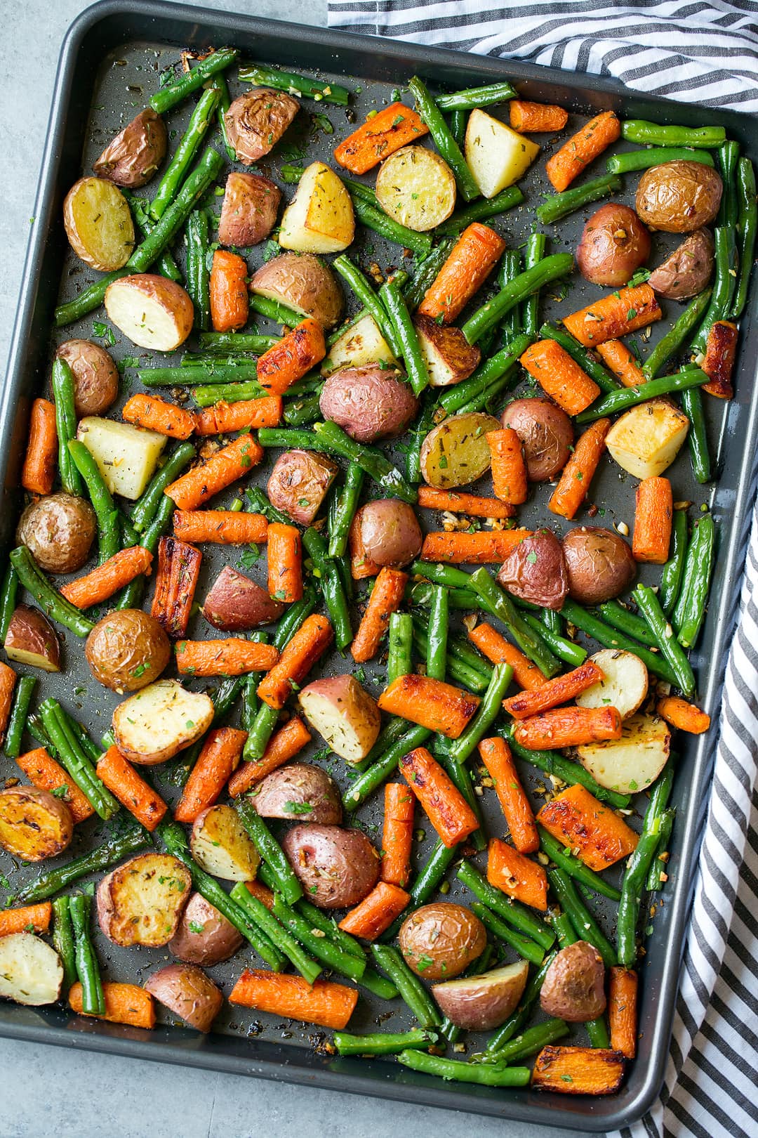 Roasted Vegetables including potatoes carrots and green beans with garlic herb seasoning. Shown here on a dark sheet pan after roasting.