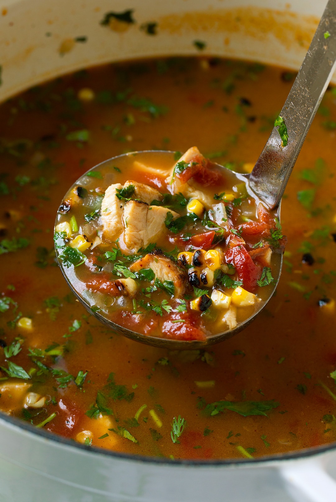 Traditional tortilla soup gets an upgrade with grilled chicken, grilled corn and plenty of diced avocados! Such a delicious summer soup! | Chicken Soup | Tortilla Soup | #cookingclassy #soup #chicken #comfortfood A ladle of Grilled Chicken Tortilla Soup