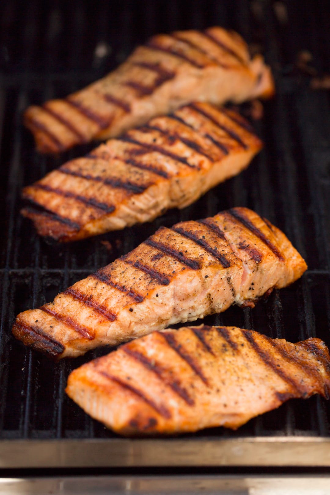Four salmon fillets pictured here on a grill.